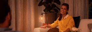 “溫暖的 LED 檯燈營造出舒適的客廳氛圍，照亮穿著黃色毛衣的女士享受晚間談話。”